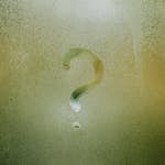 A question mark drawn on foggy glass, evoking curiosity and mystery.