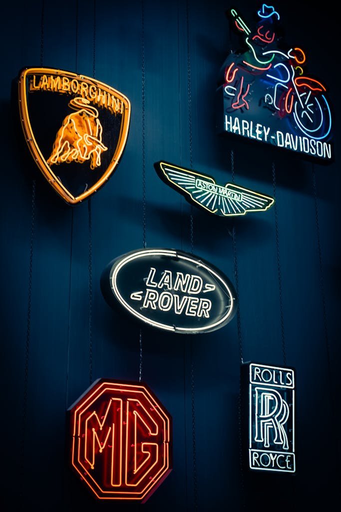 Vibrant neon signs showcasing luxury vehicle brands and logos in a dark, moody setting.