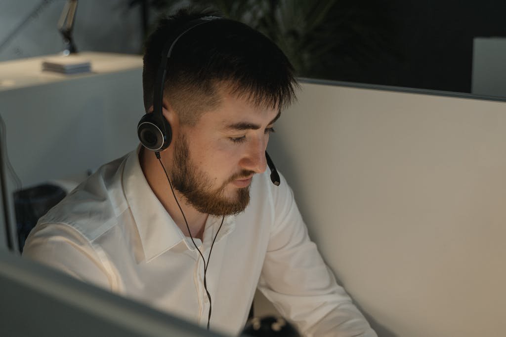 A bearded man with a headset working attentively in a call center.