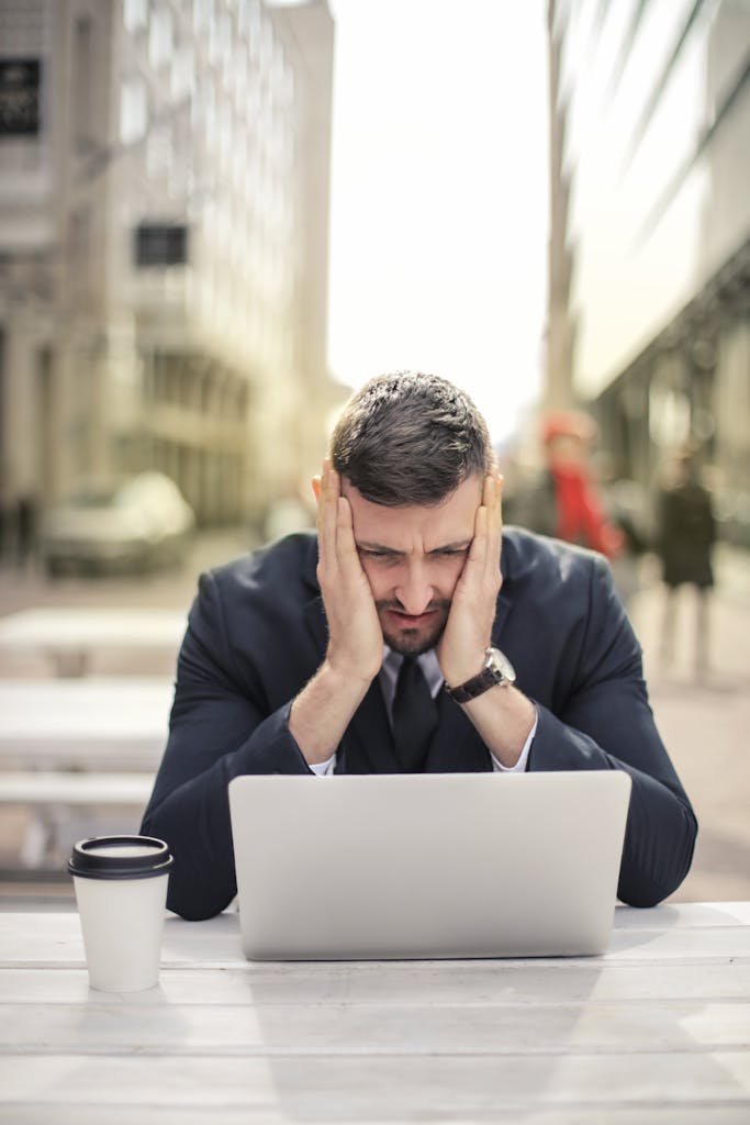 Businessman looking stressed while working on laptop outdoors in city environment.